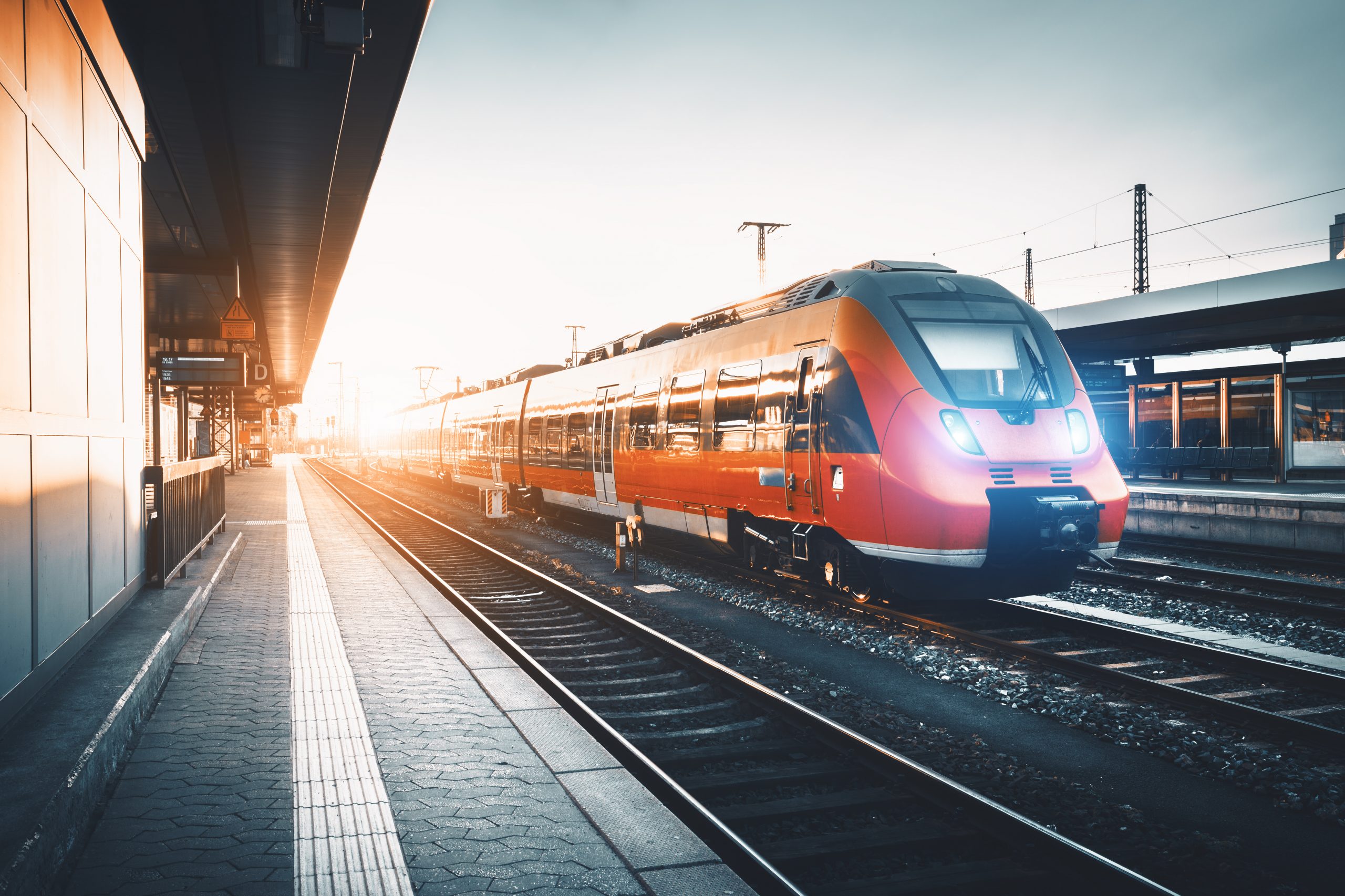 Modern high speed red commuter train at the railway station at sunset. Turning on train headlights. Railroad with vintage toning. Train at railway platform. Industrial landscape. Railway tourism