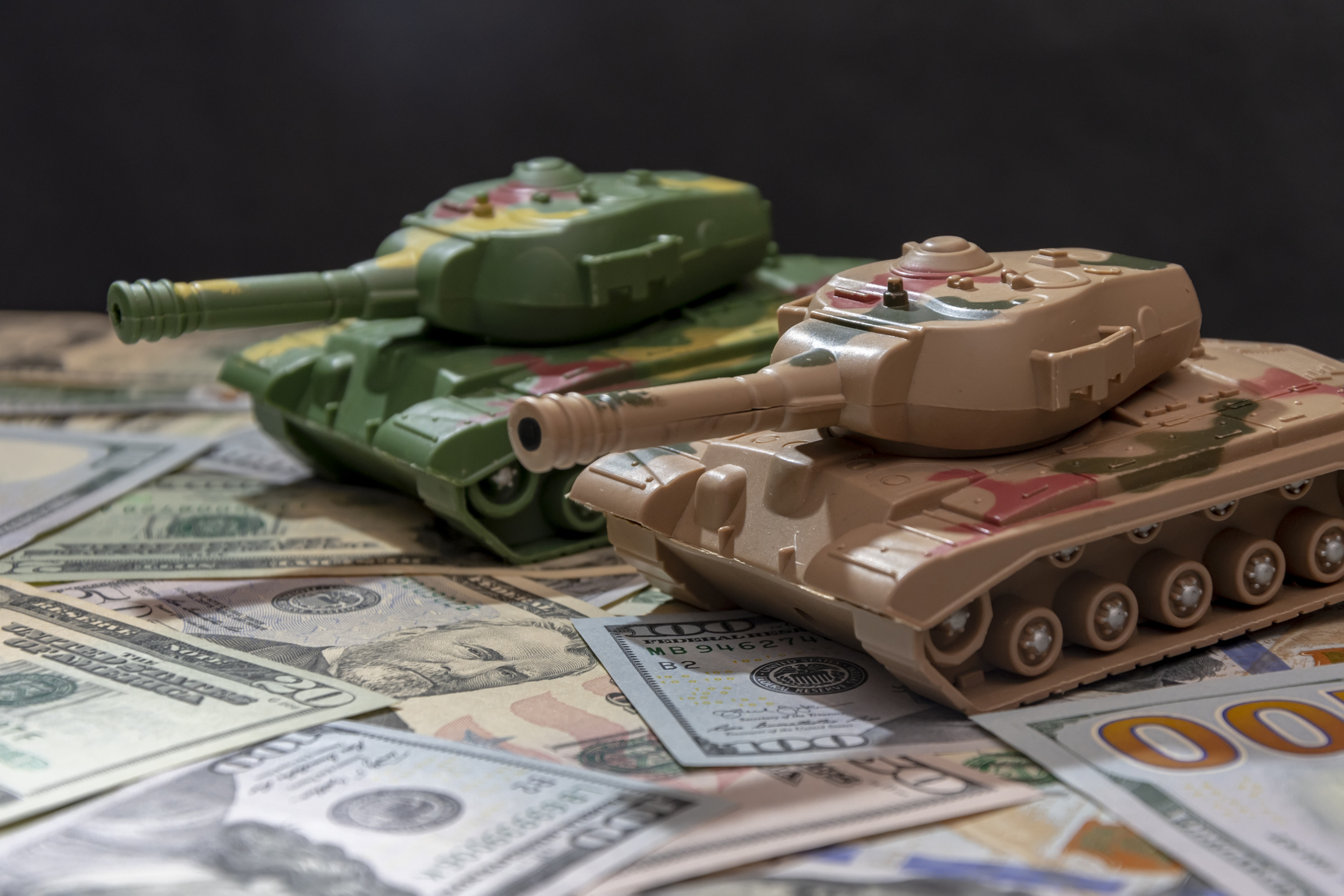 Two tanks against a backdrop of American money, emphasising the financial implications of military conflicts.